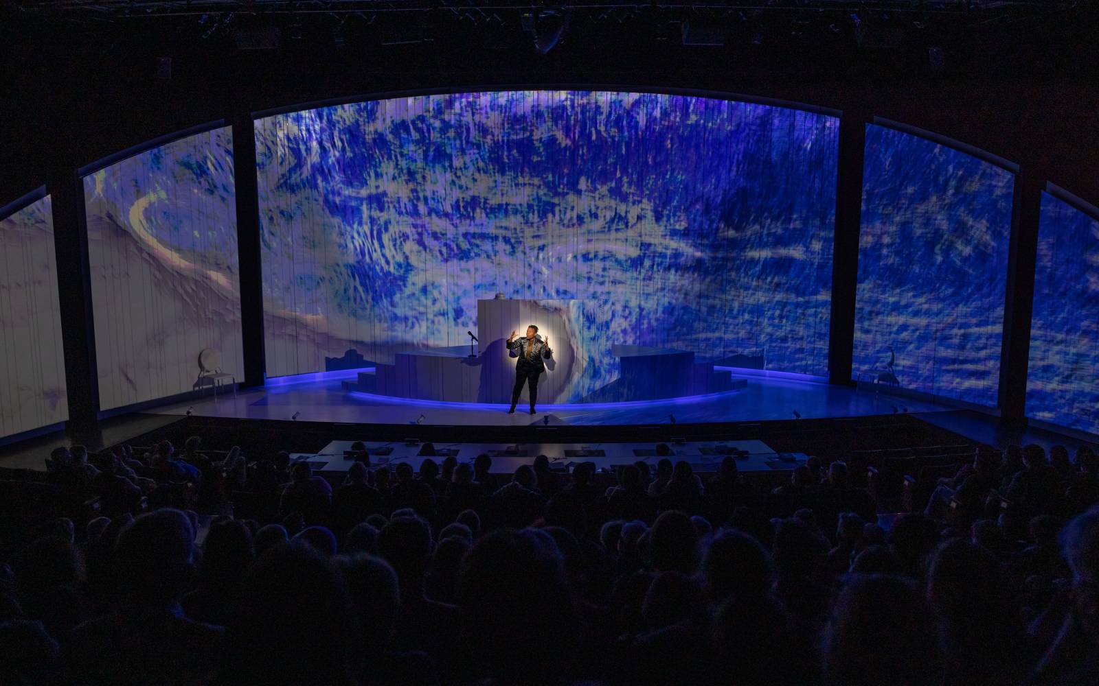 Jennifer Kidwell in Ocean Filibuster spotlit against a stage with waves projected on it.