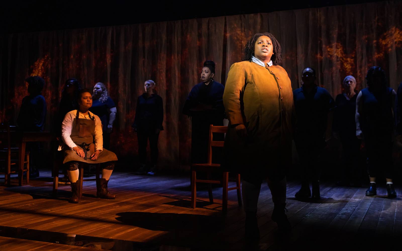 Tiffani Barbour seated to the left, and members of the company in the background, watch Salome B. Smith.