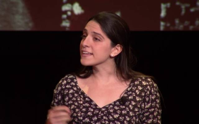 Sammi Cannold in a floral blouse on a darkened stage.