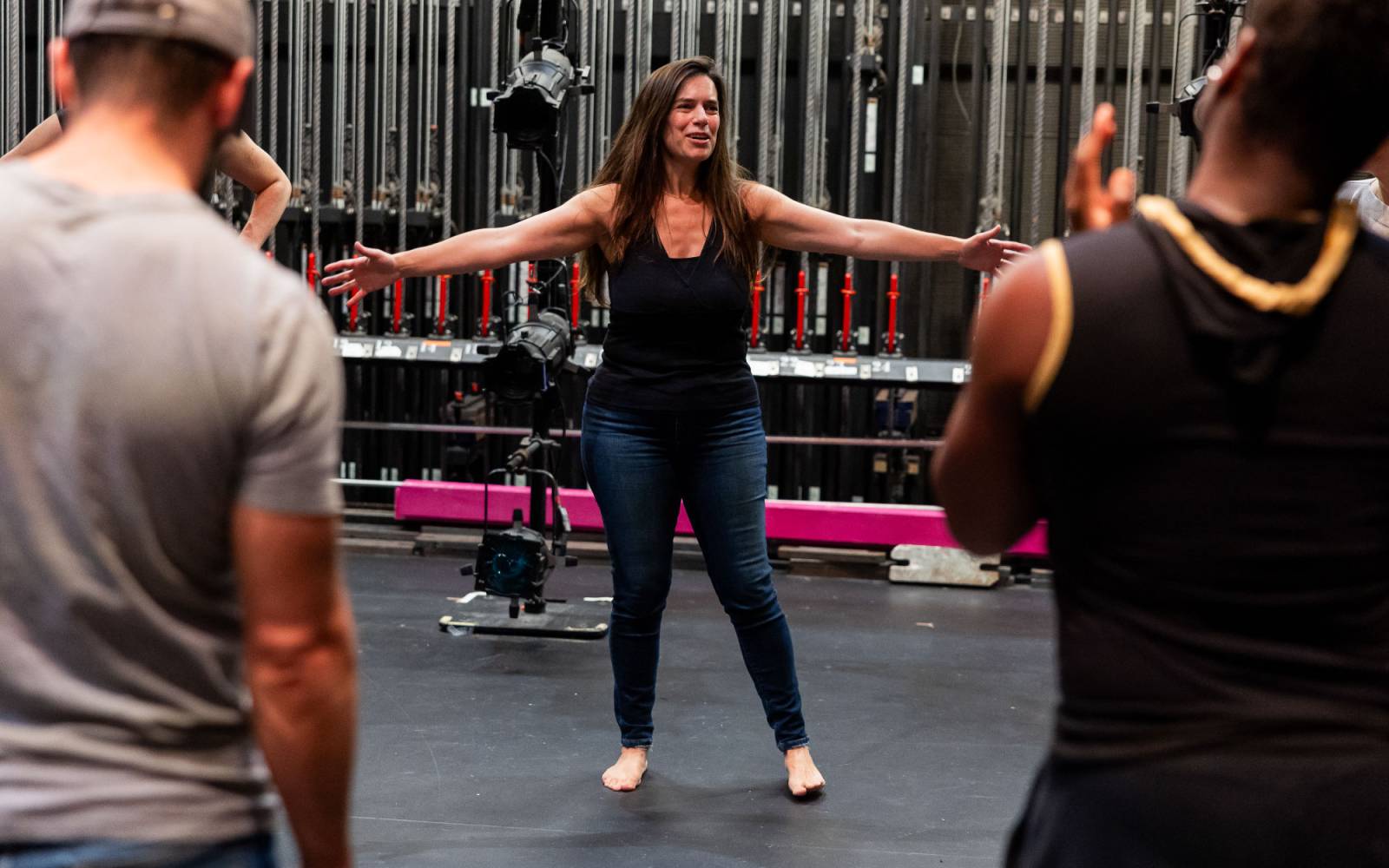 Shana Cooper stretches her arms out towards members of the cast, watching on.