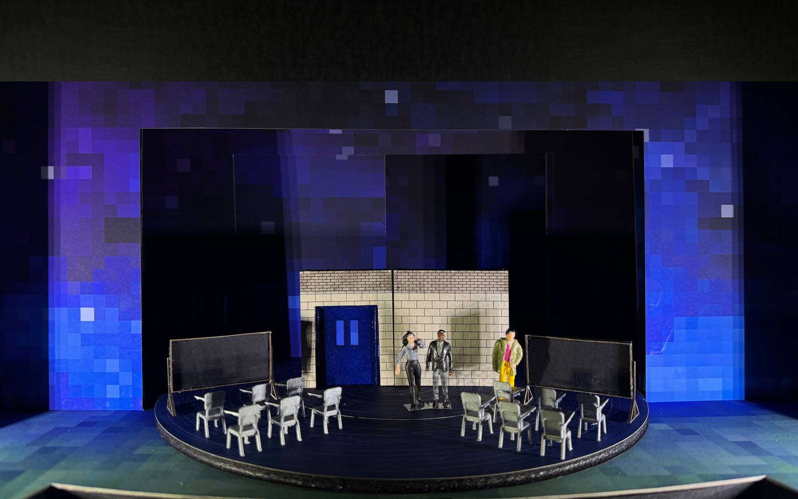 Set model of Wonder with two sets of six chairs facing blackboards, with three figurines standing in front of a cinderblock wall.