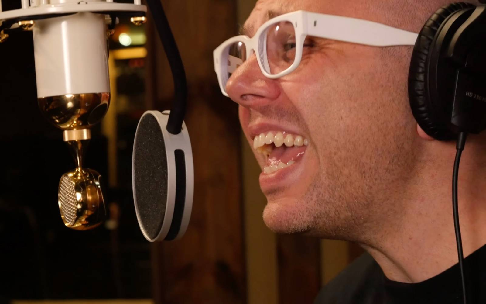 Ian Axel in white glasses sings into a studio microphone.